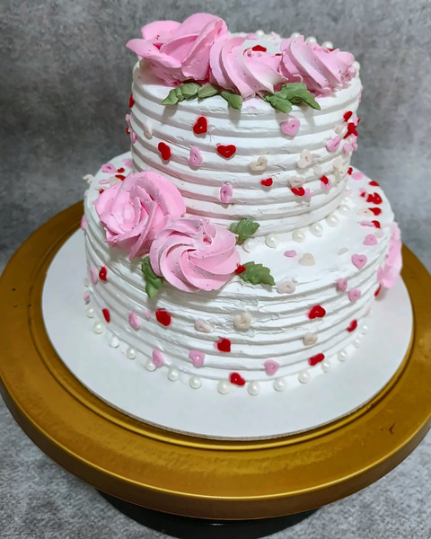 Two-tier white cake with pink piped roses and heart sprinkles